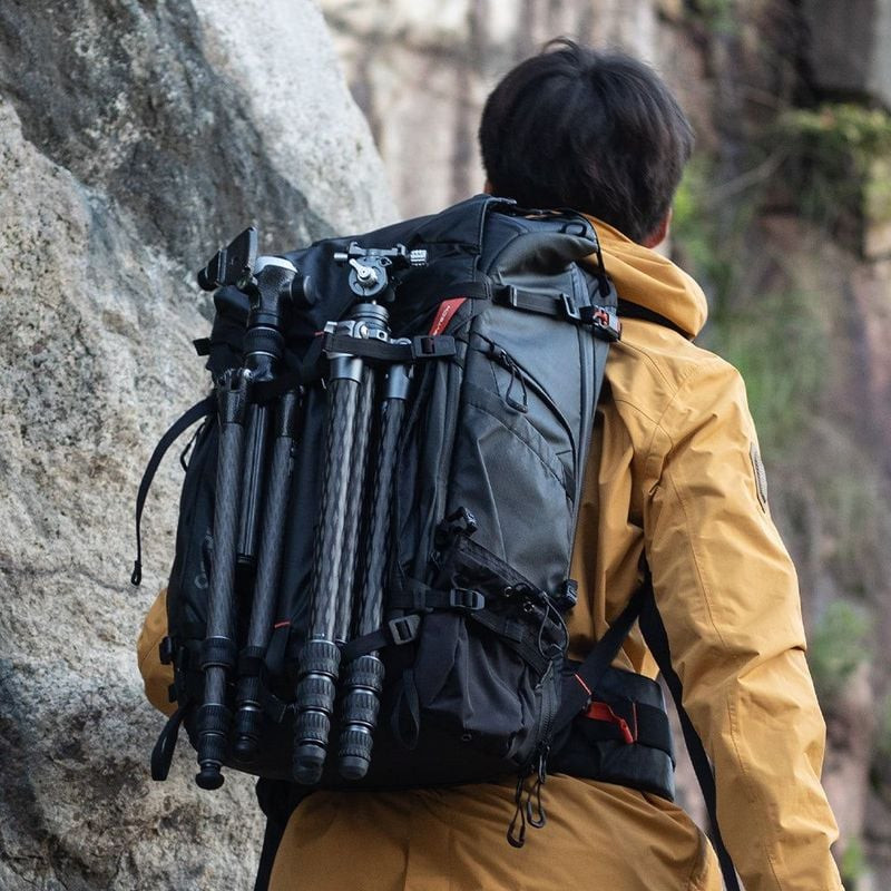 Randonneur portant le sac à dos PGYTECH OnePro Focux 25L Space Black chargé de trépieds, debout sur 