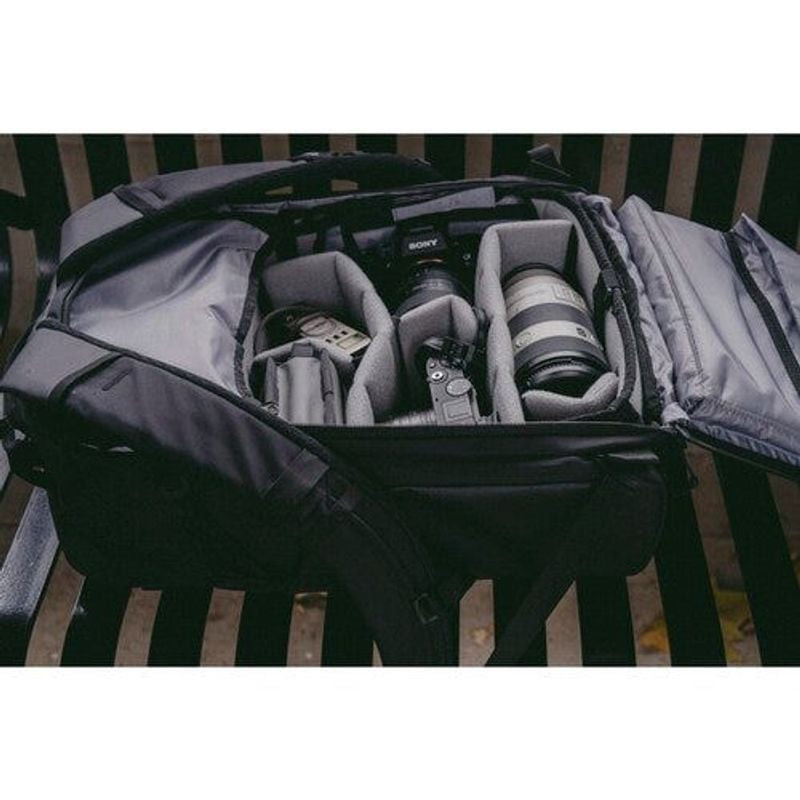 Sac à dos WANDRD PRVKE 31L ouvert sur un banc avec appareil photo, objectifs et séparateurs en mouss