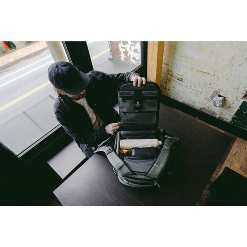 Image lifestyle d'une personne ouvrant le sac à dos WANDRD PRVKE 21L sur une table, révélant les com