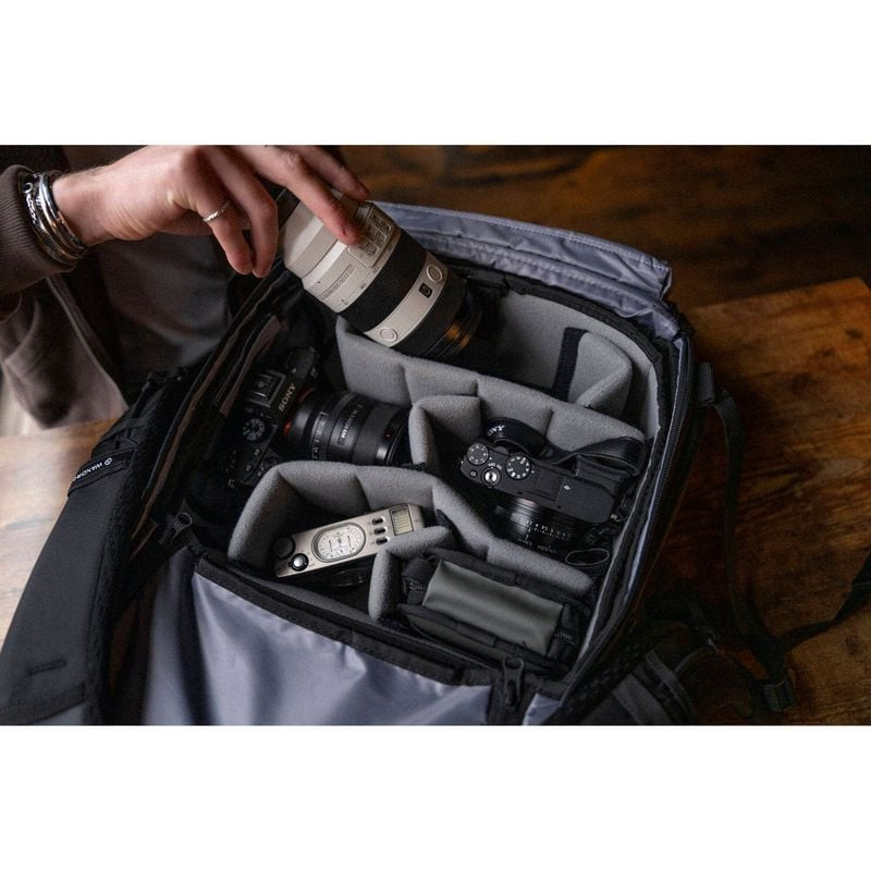 Mains chargeant objectifs et boîtier photo dans le compartiment caméra ouvert du sac WANDRD PRVKE 21