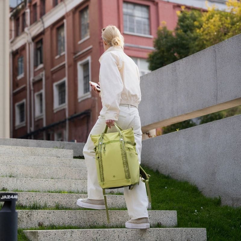 Femme portant le PGYTECH OneGo Roamer Tote 18L vert par la poignée dans les escaliers urbains