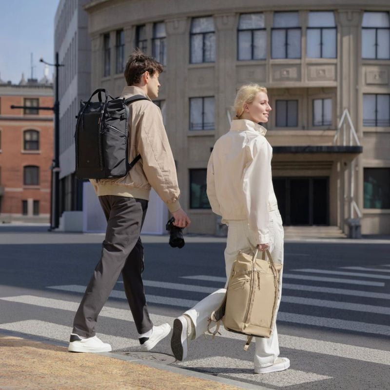 Un homme porte le sac à dos PGYTECH OneGo Roamer noir, une femme un tote Sable sur un passage piéton
