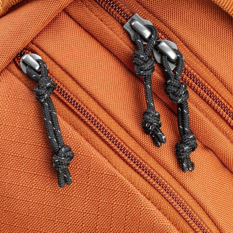 Gros plan des tirettes de zip du Think Tank TurnStyle 8L Urban Rust, cordon noir noué et glissières 