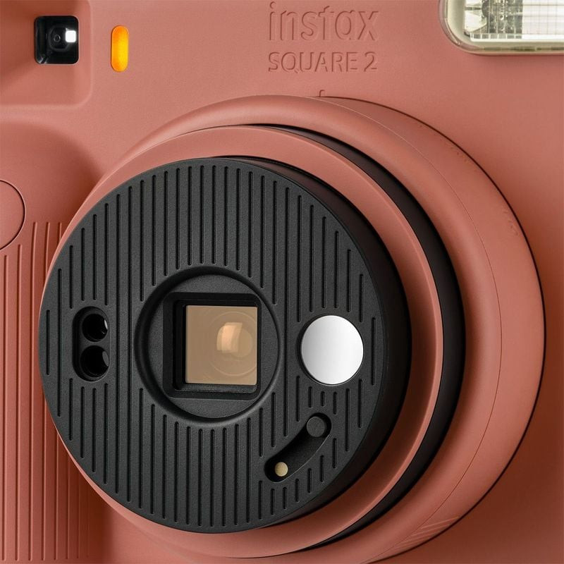 Gros plan du barillet d'objectif noir de l'Instax Square 2, miroir selfie et flash sur le boîtier ro